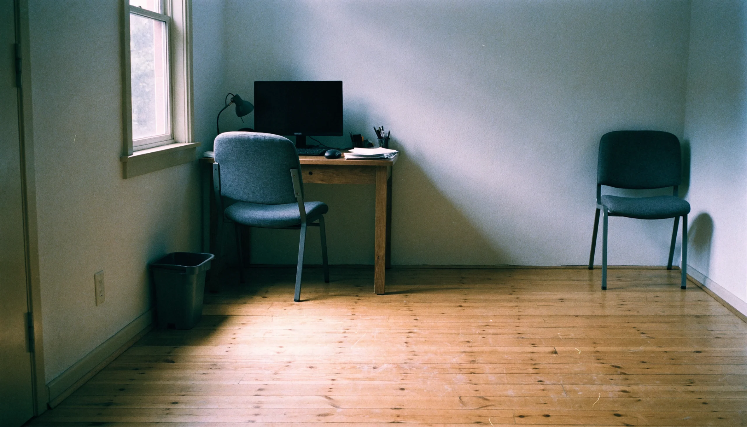 A one-person office with a single desk and work chair, and a second identical chair standing unused against the far wall